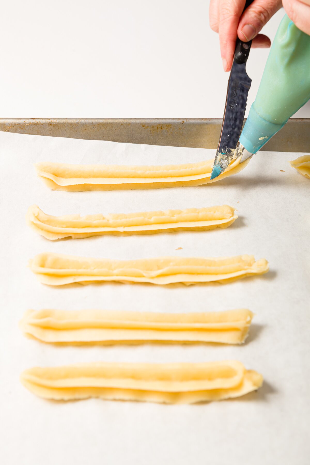 Piping churros onto a piece of parchment and cutting with a knife