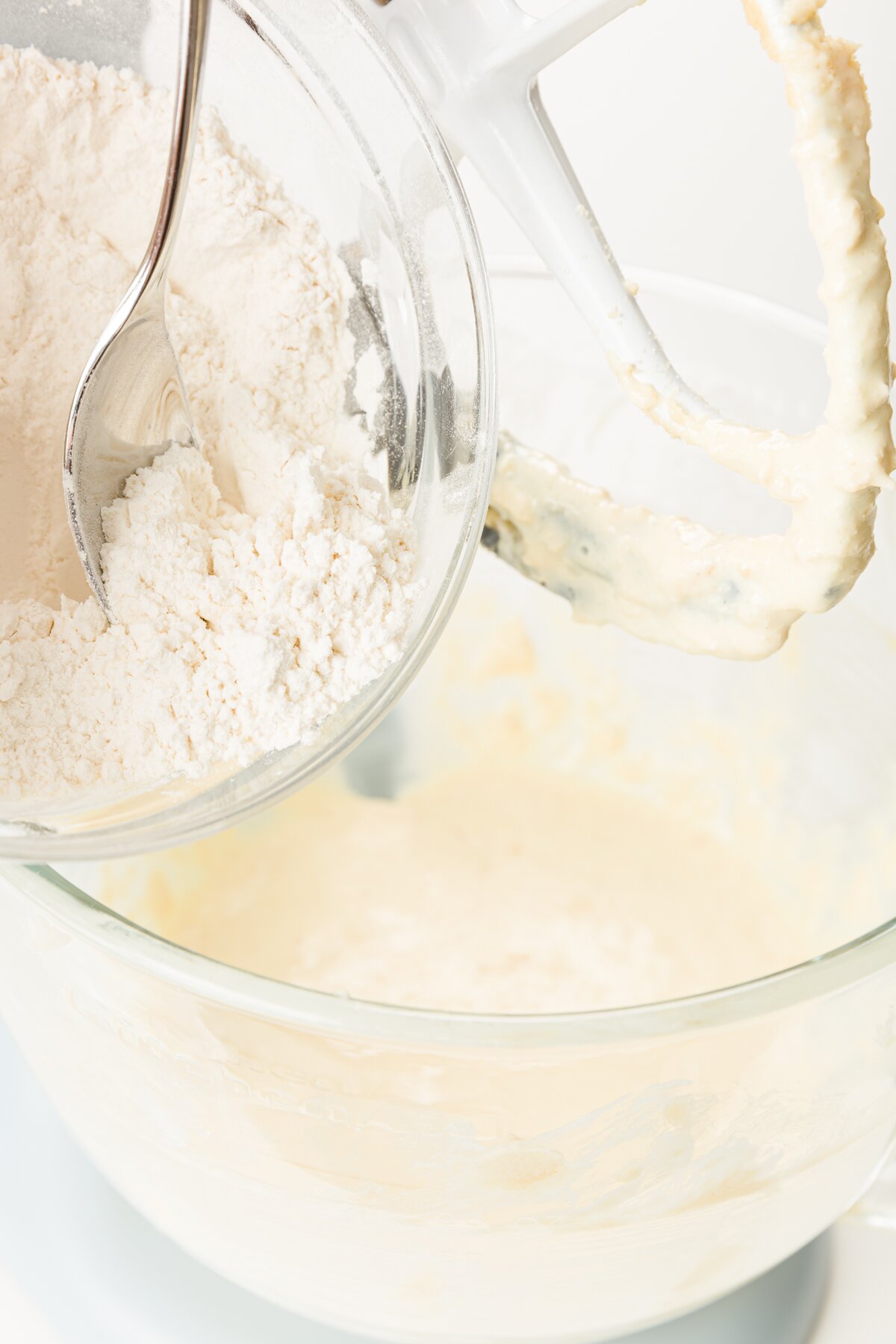 Adding flour to KitchenAid mixing bowl with wet ingredients inside