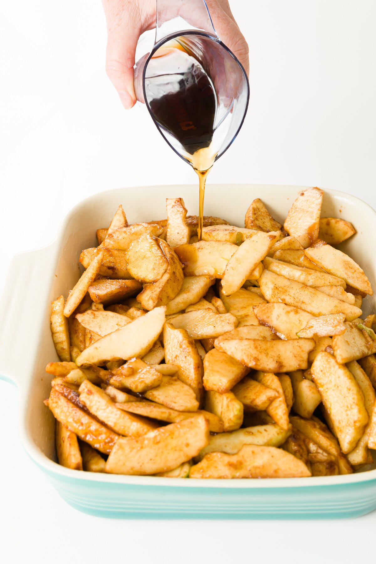 Pouring maple syrup over apples in a blue baking pan