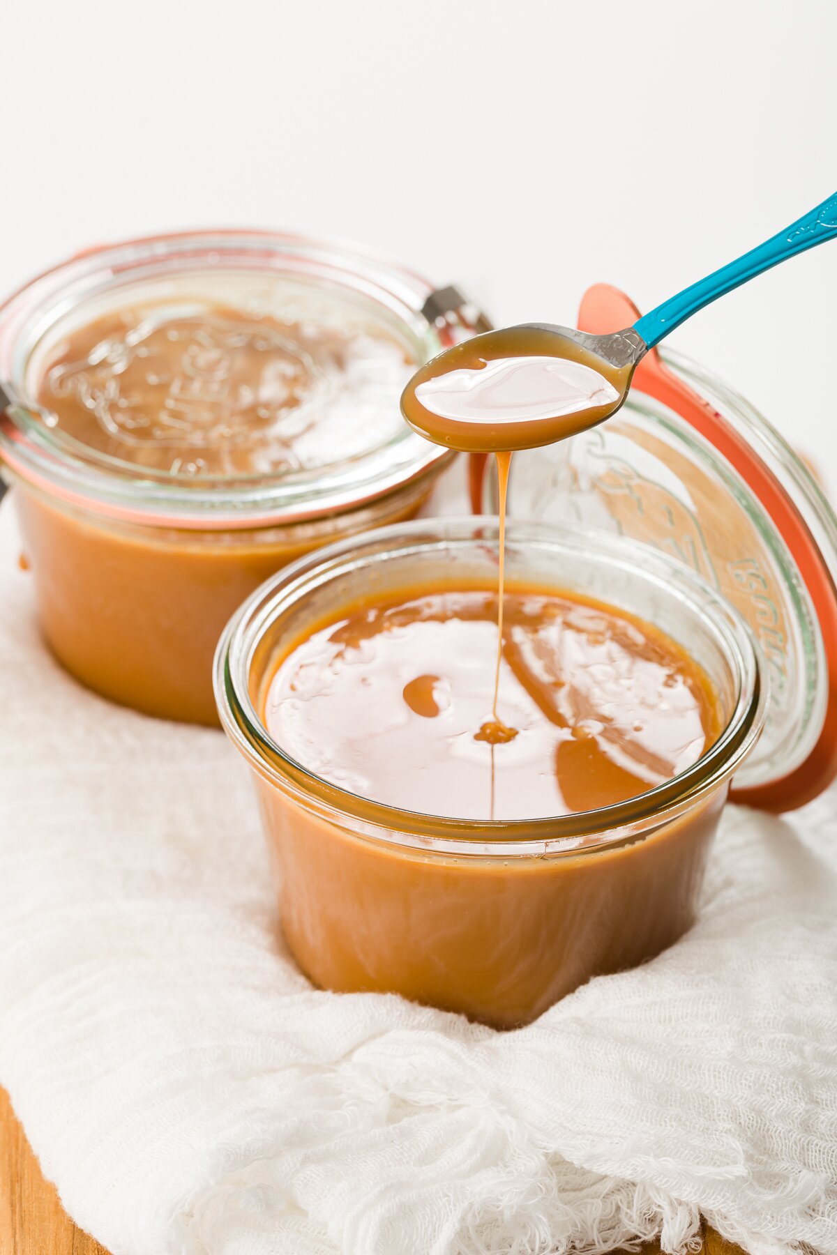 two jars of cajeta with a spoon full of the caramel hovering over one