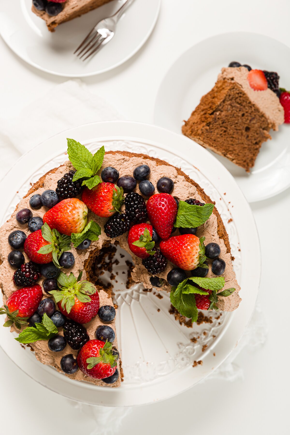 Overhead shot of angel food cake topped with berries and fresh mint with slices of cake next to it 
