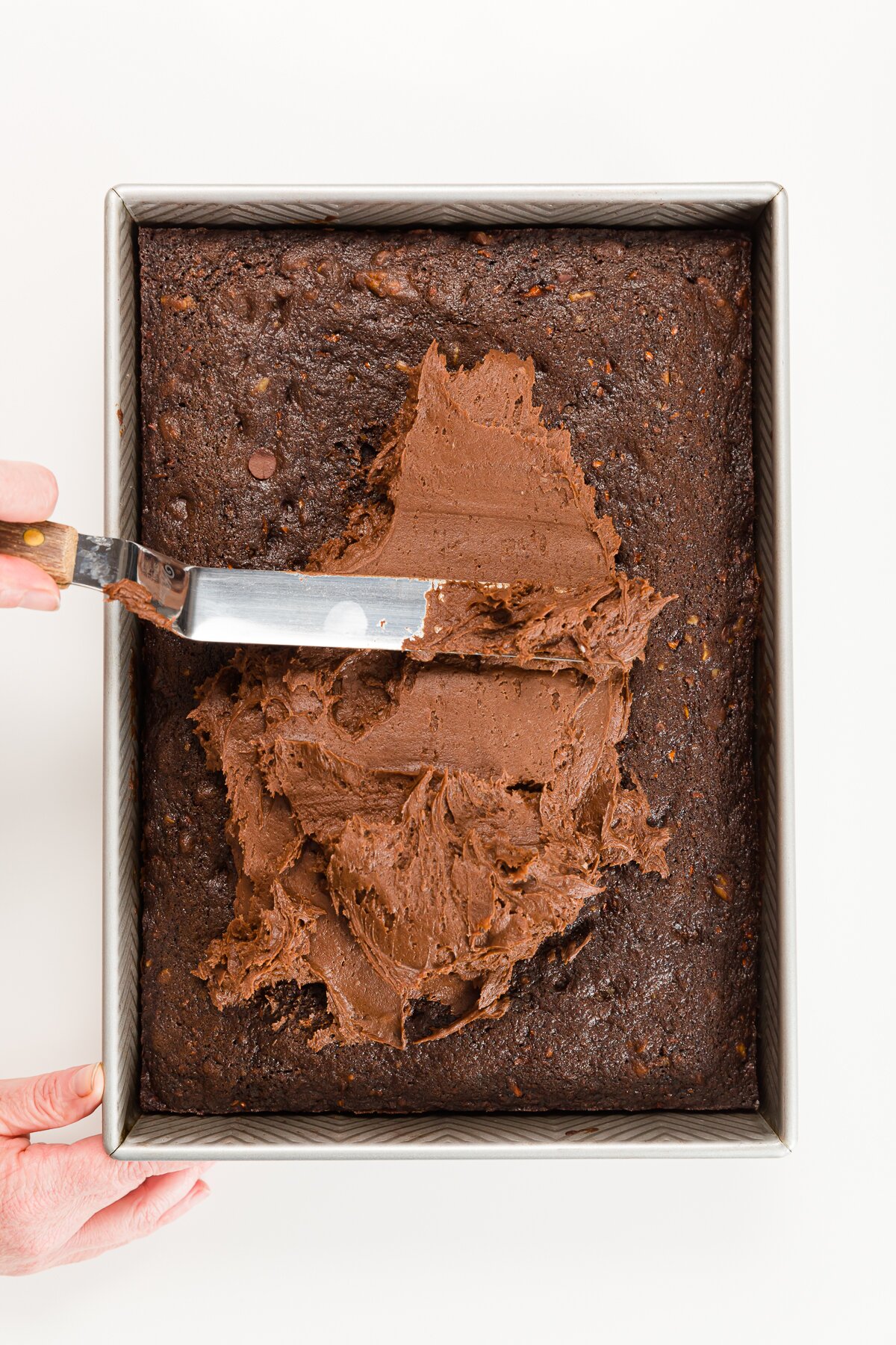 Spreading chocolate cream cheese frosting on chocolate carrot cake