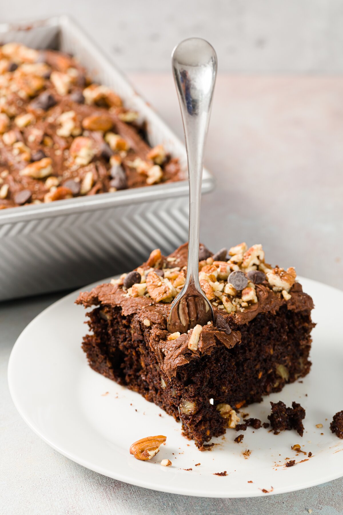 Piece of chocolate carrot cheesecake on a white plate with a fork in it and the baking dish in the background