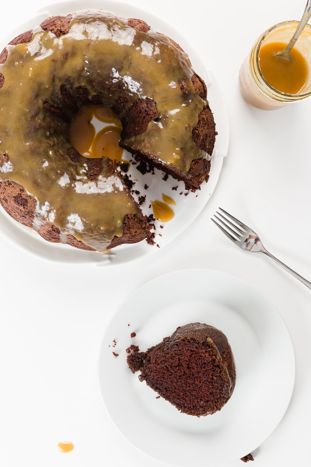 Top down shot of chocolate whiskey cake with slice pulled out on a plate and jar of whiskey sauce