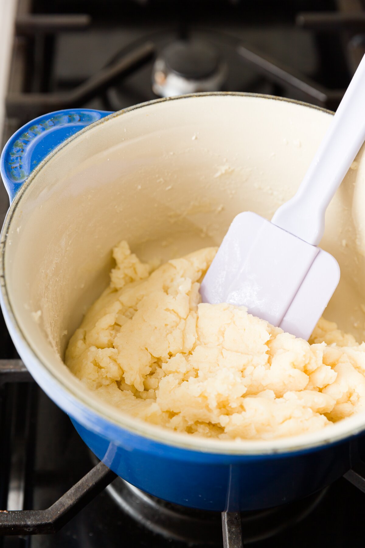 Thick dough in a blue pot with a purple spatula in it