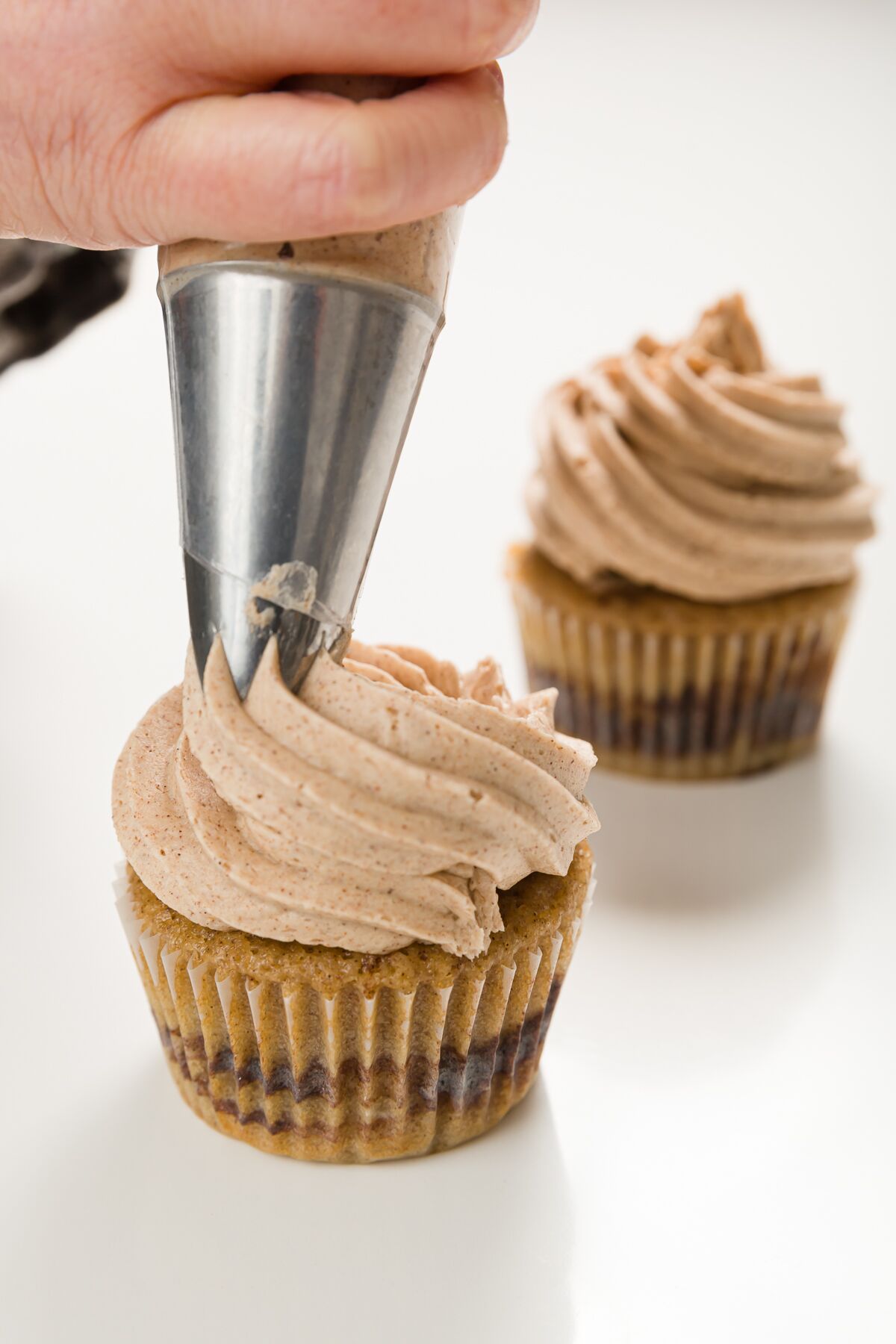 Piping cinnamon buttercream onto cupcakes