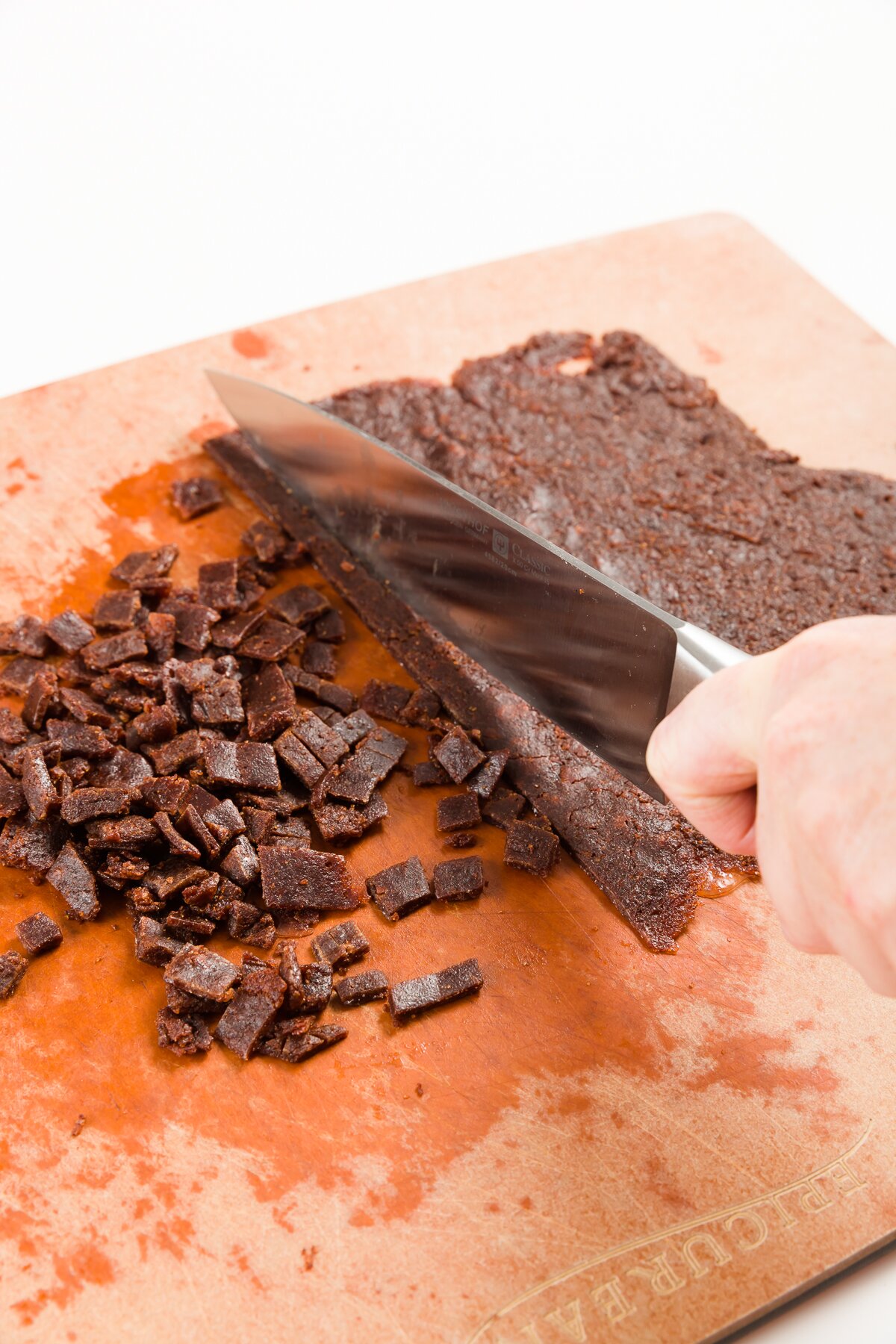 Chopping cinnamon chips on a brown cutting board with a chef's knife