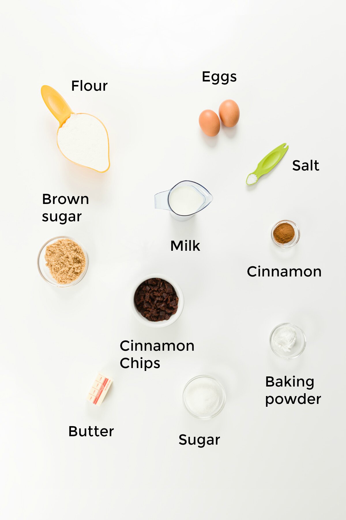 overhead photo of cinnamon muffin ingredients, labeled: flour, eggs, brown sugar, milk, salt, cinnamon, cinnamon chips, butter, sugar, and baking powder