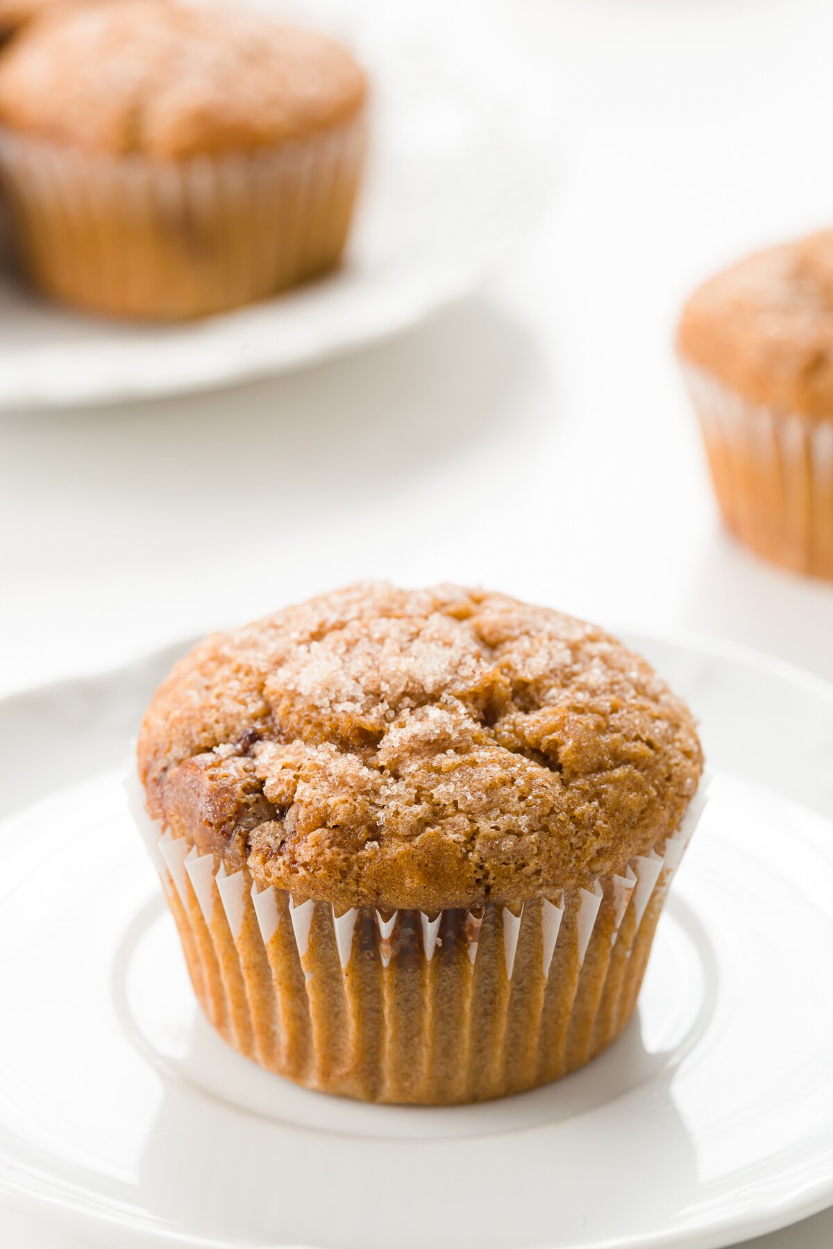 cinnamon muffin on a white plate with other muffins in the background