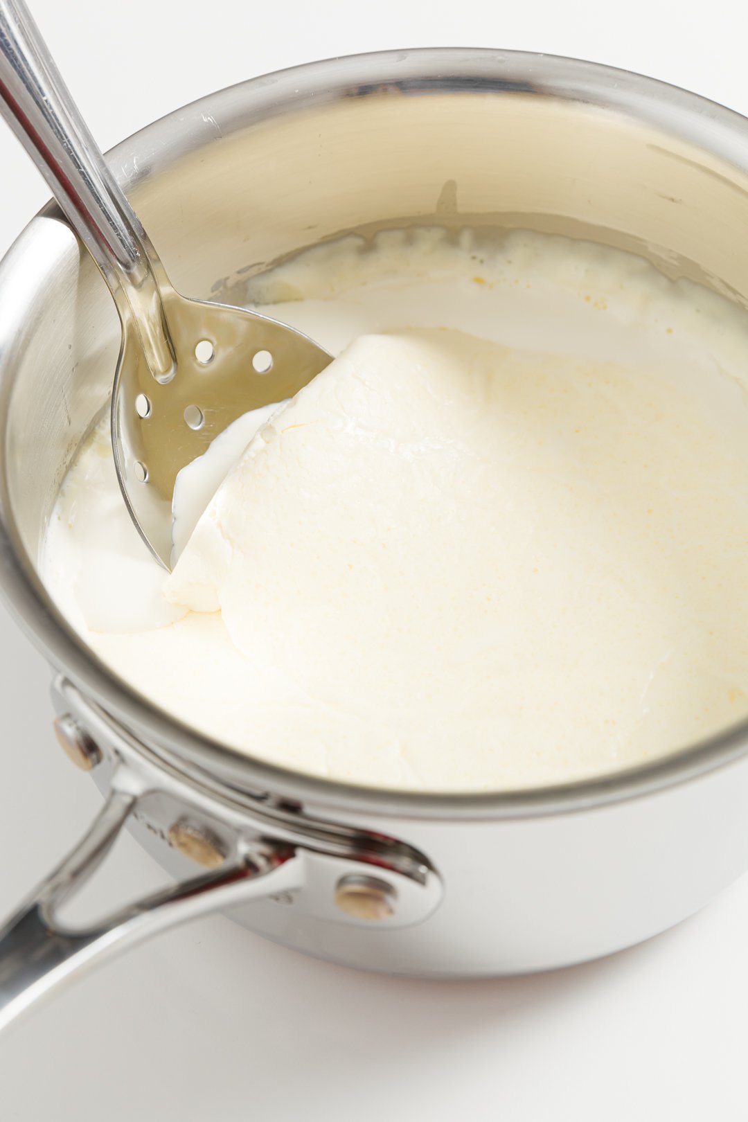 Skimming clotted cream in a pot using a slotted spoon