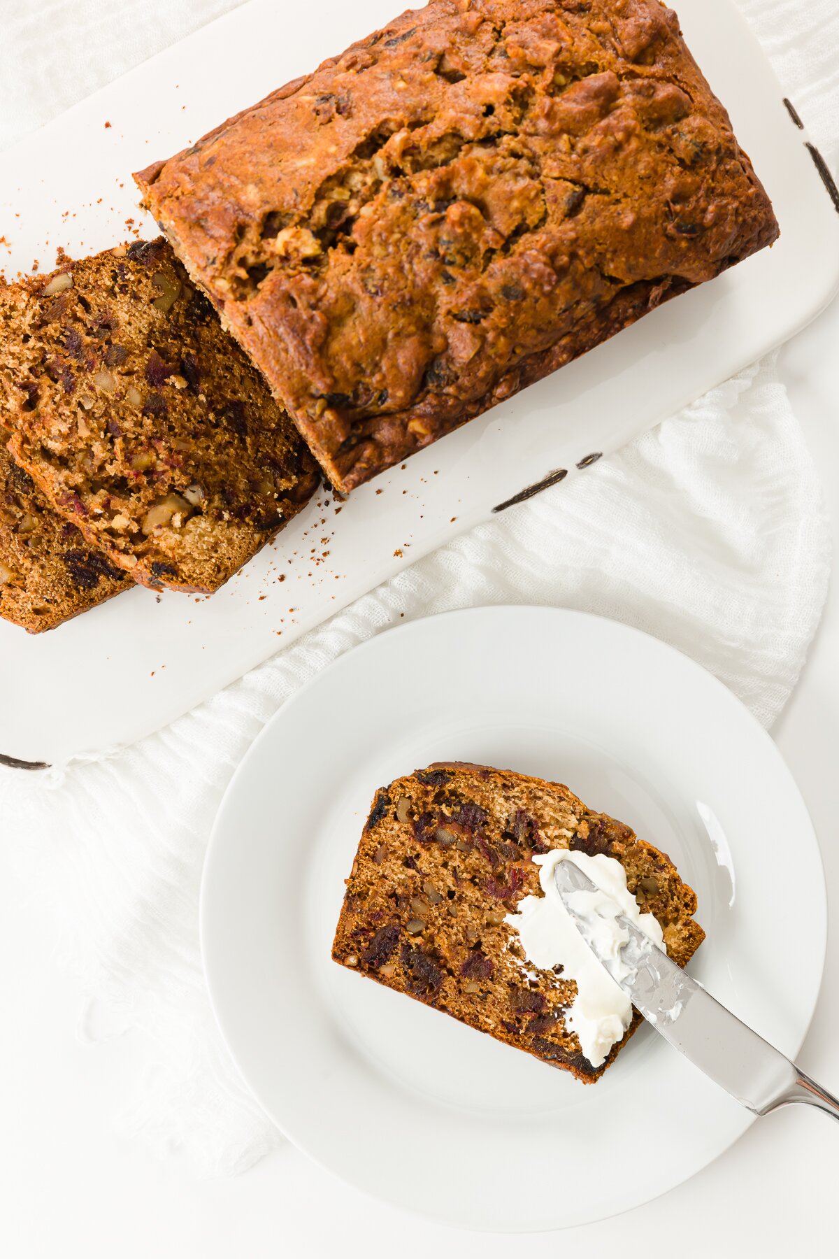 Spreading cream cheese on a slice of bread with a loaf in the background