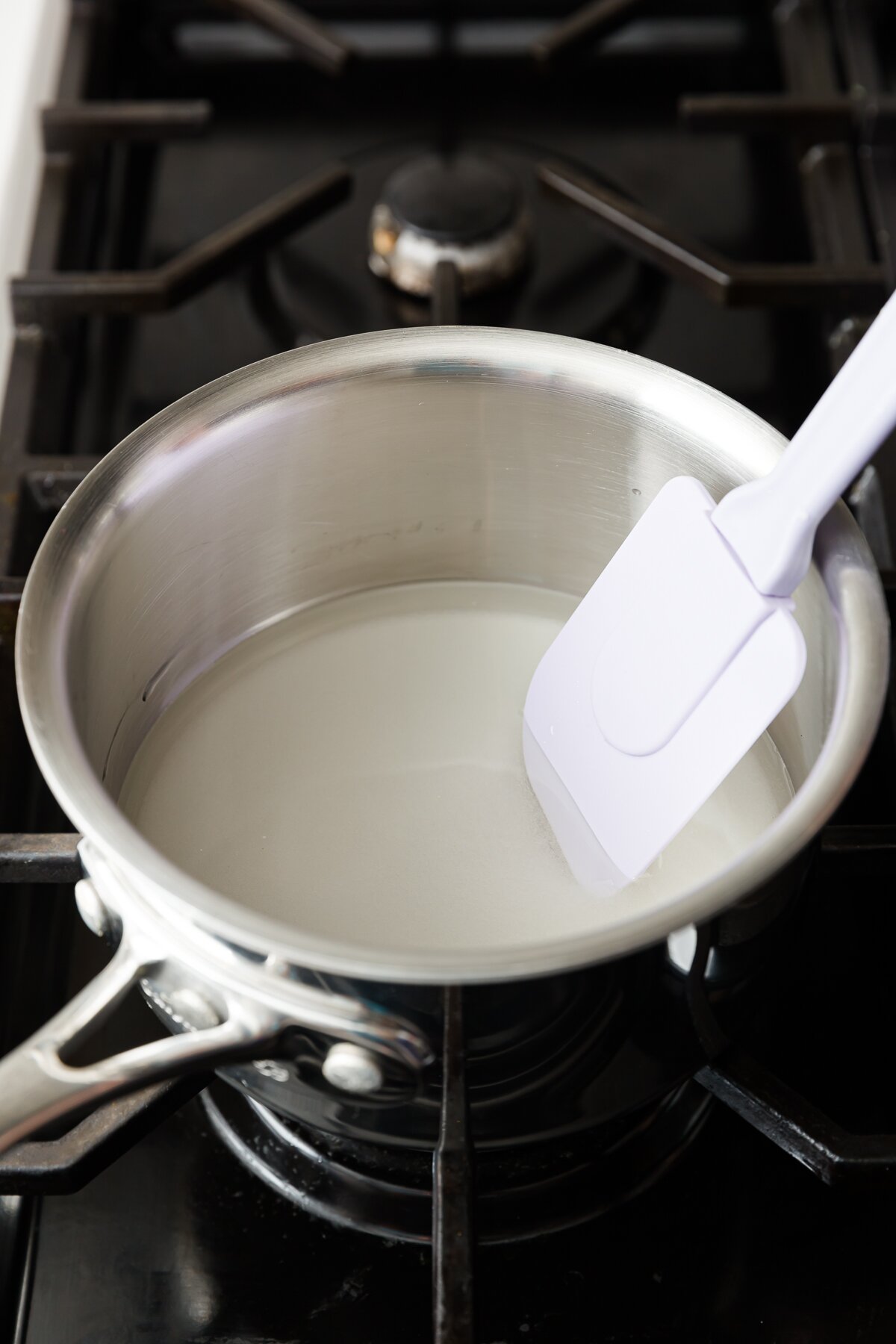 Sugar syrup in a saucepan on the stove with a purple spatula
