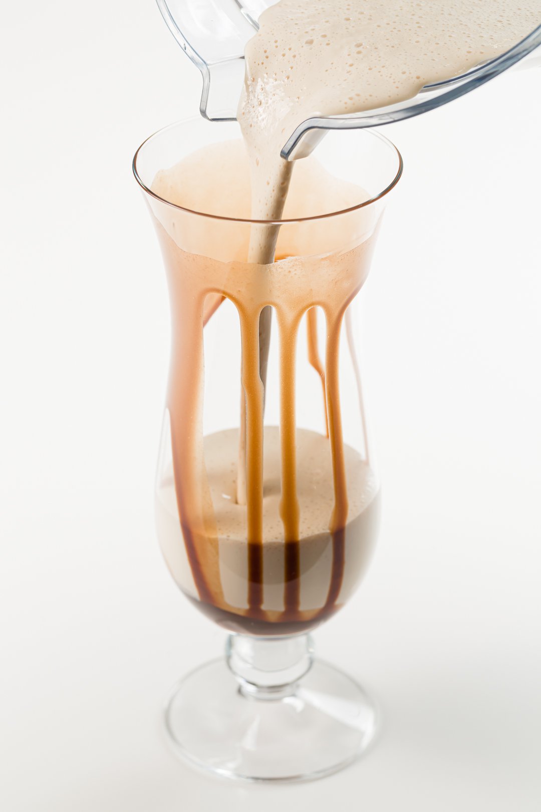 pouring from a pitcher of frozen mudslide cocktails into a glass drizzled with chocolate sauce