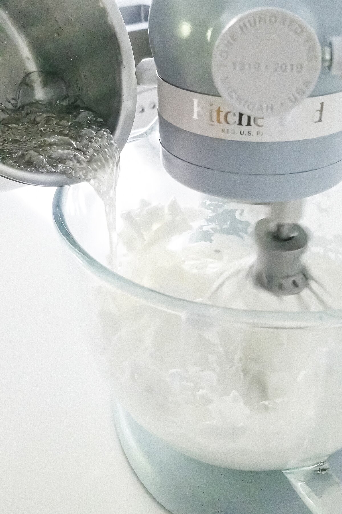 pouring hot sugar syrup into the bowl of a stand mixer