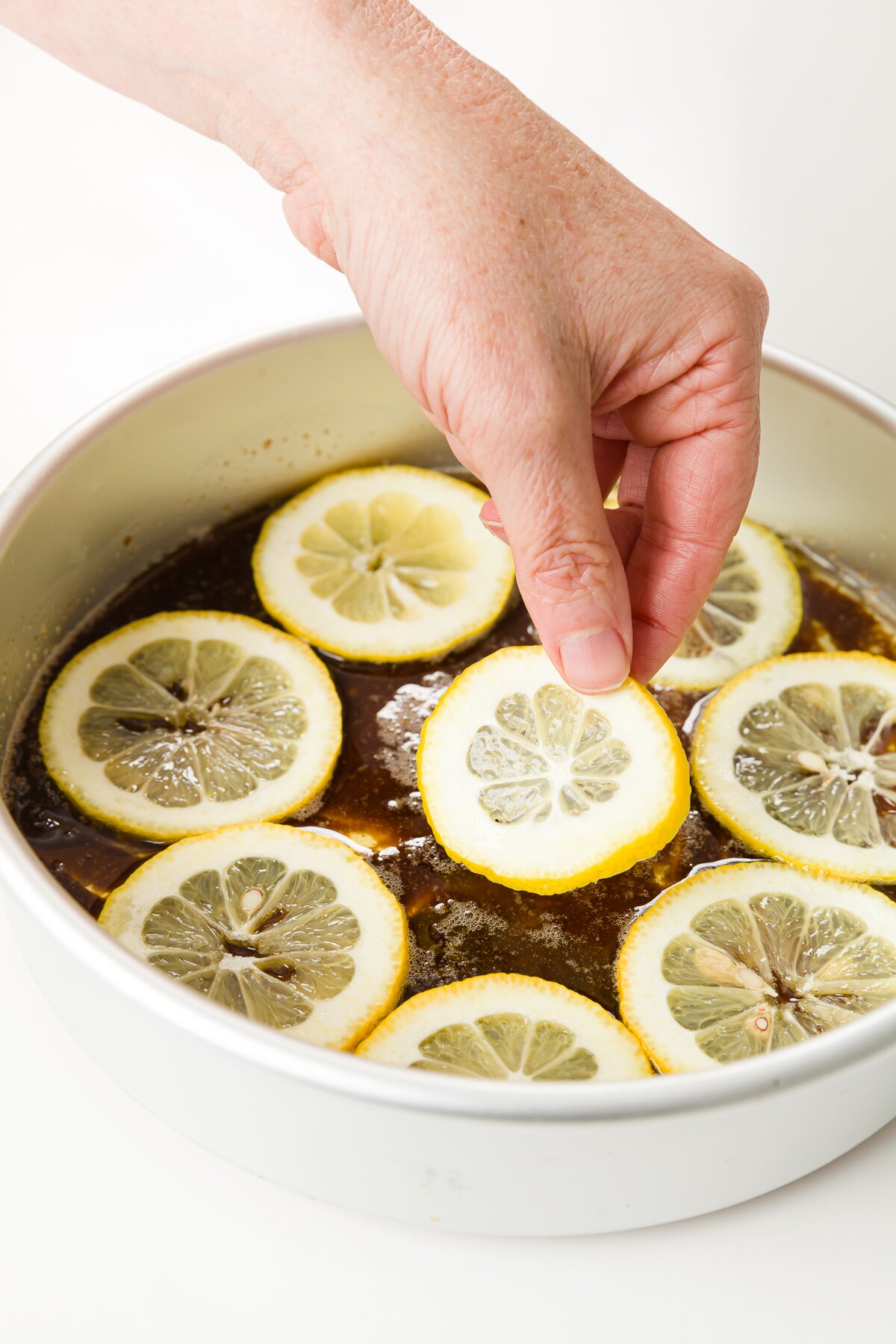 hand placing a lemon on top of butter sugar mixture in a round cake pan