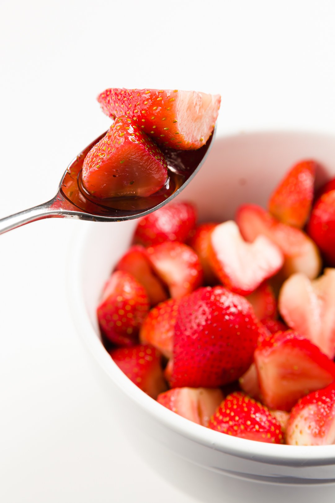 Macerated strawberries on a spoon hovering above a large bowl full of macerated strawberries