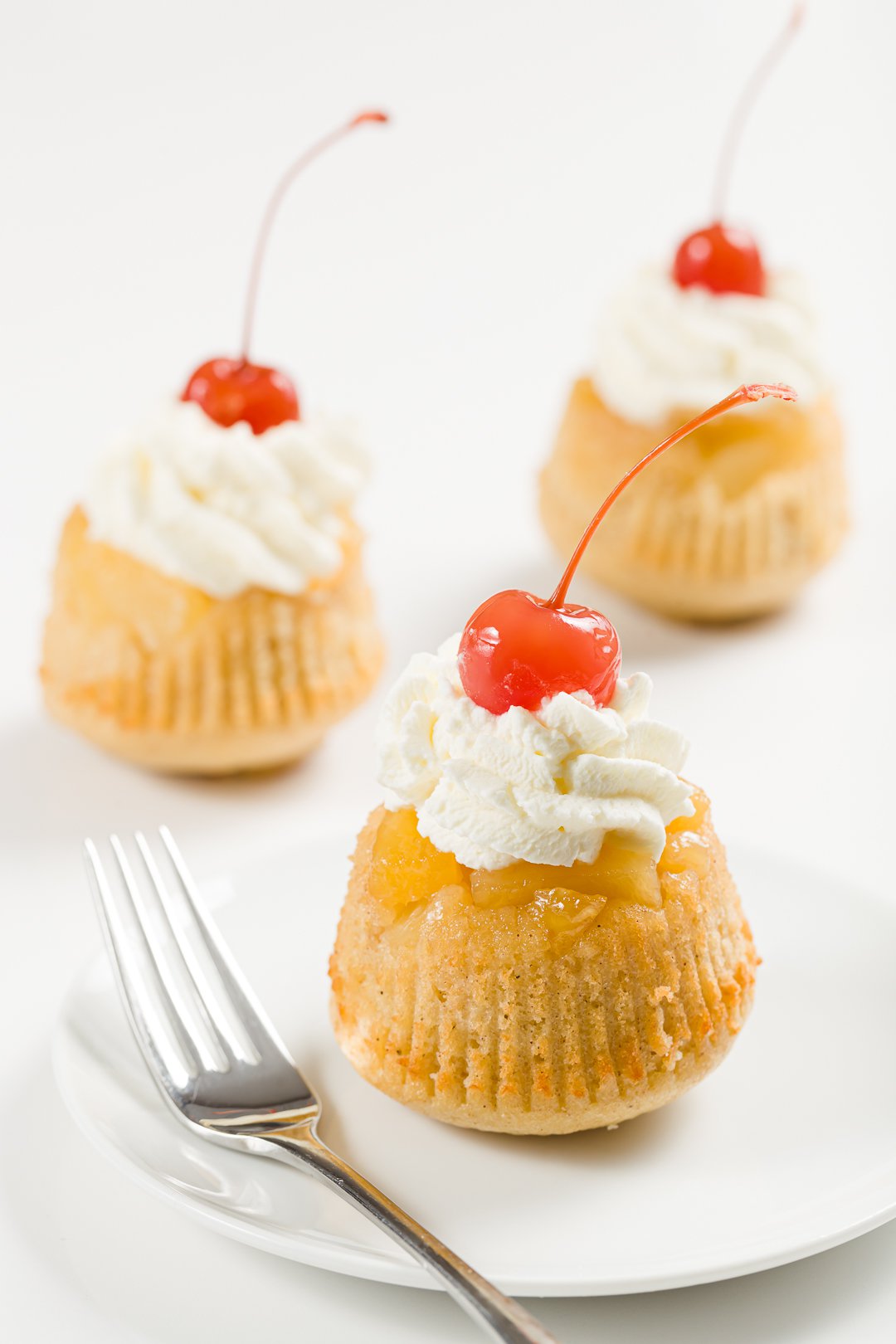 pineapple upside-down cupcakes topped with whipped cream and maraschino cherries