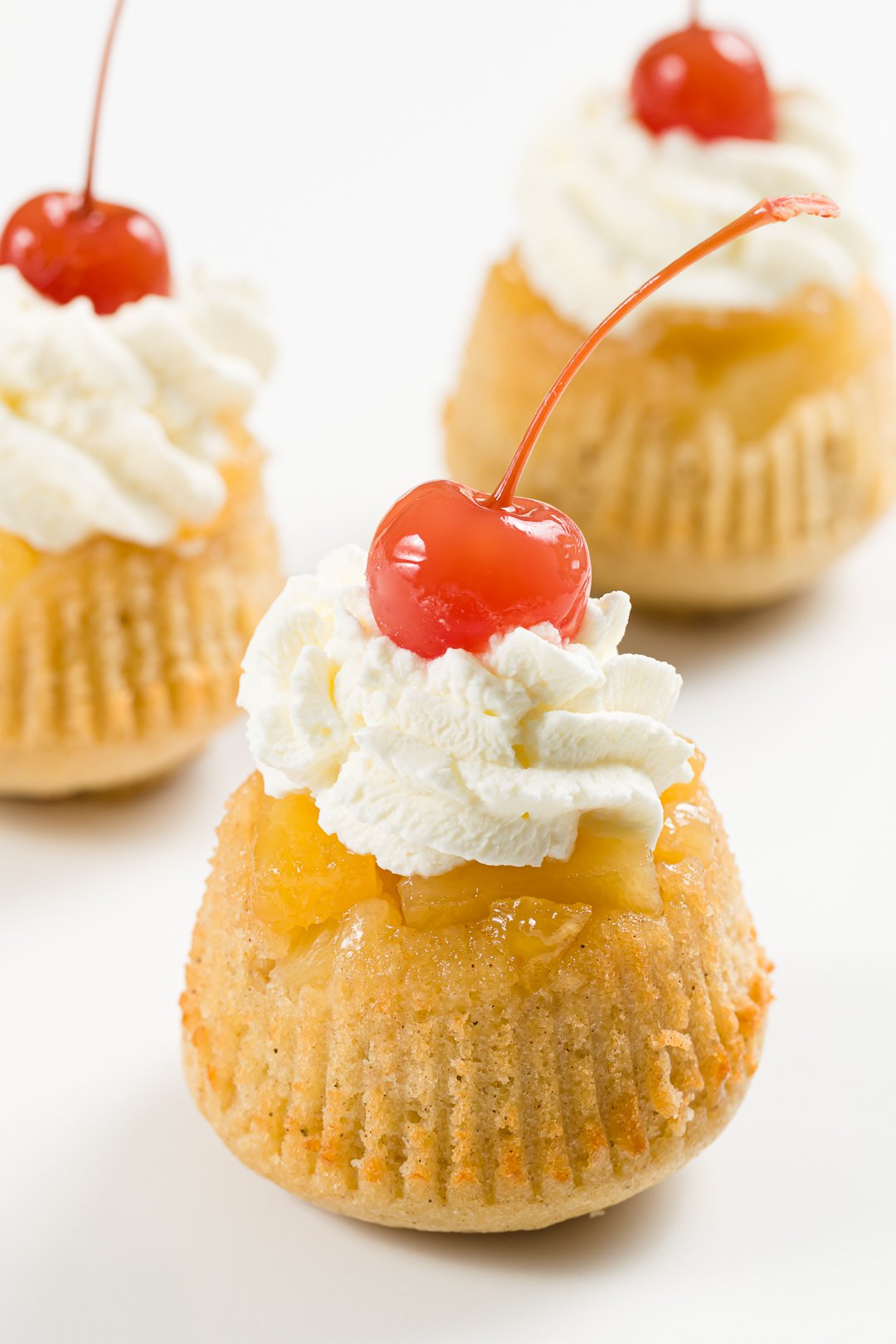 close-up view of a pineapple upside-down cupcake topped with whipped cream and a maraschino cherry
