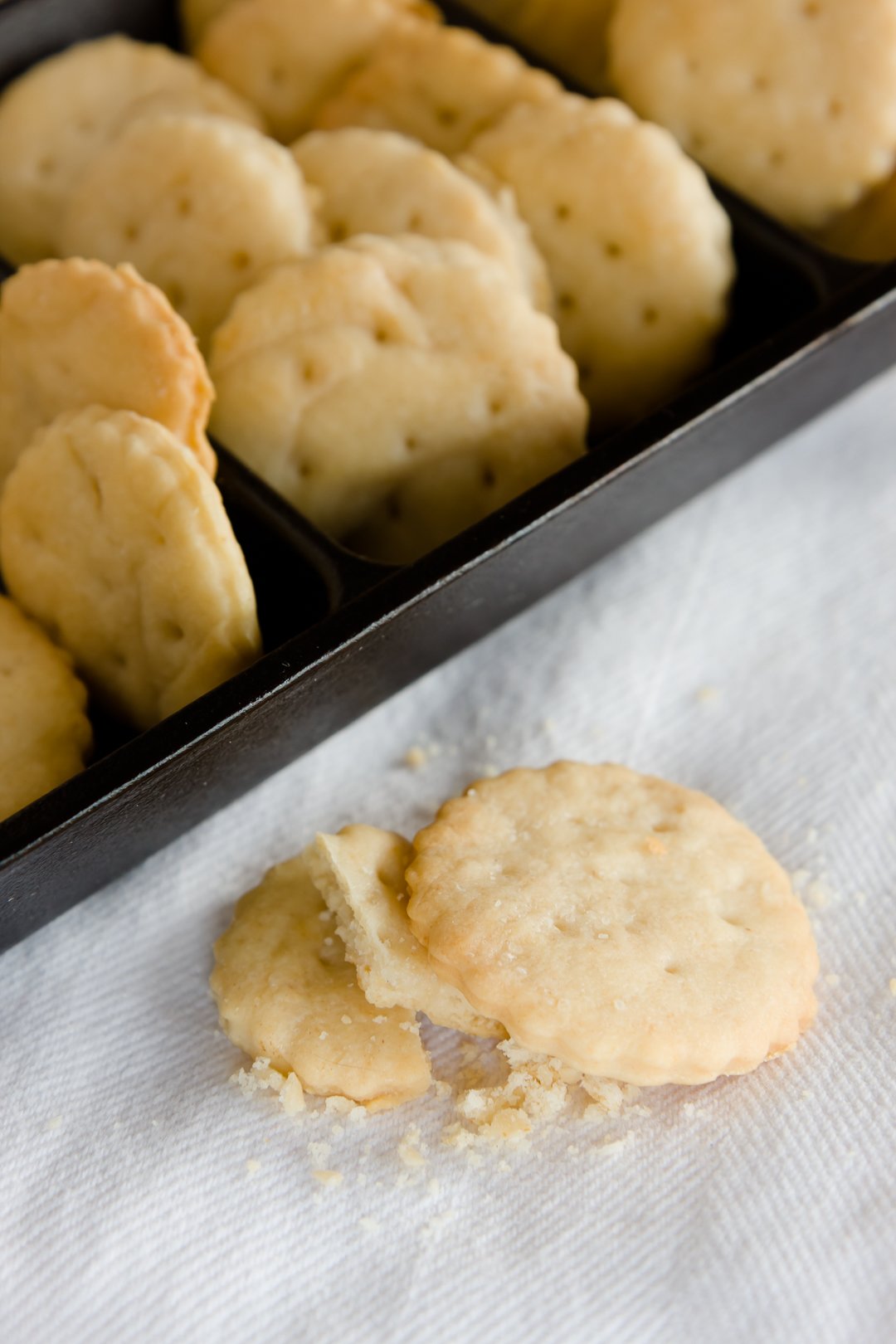 A closeup of a cracked homemade Ritz cracker with a number of others in a serving dish