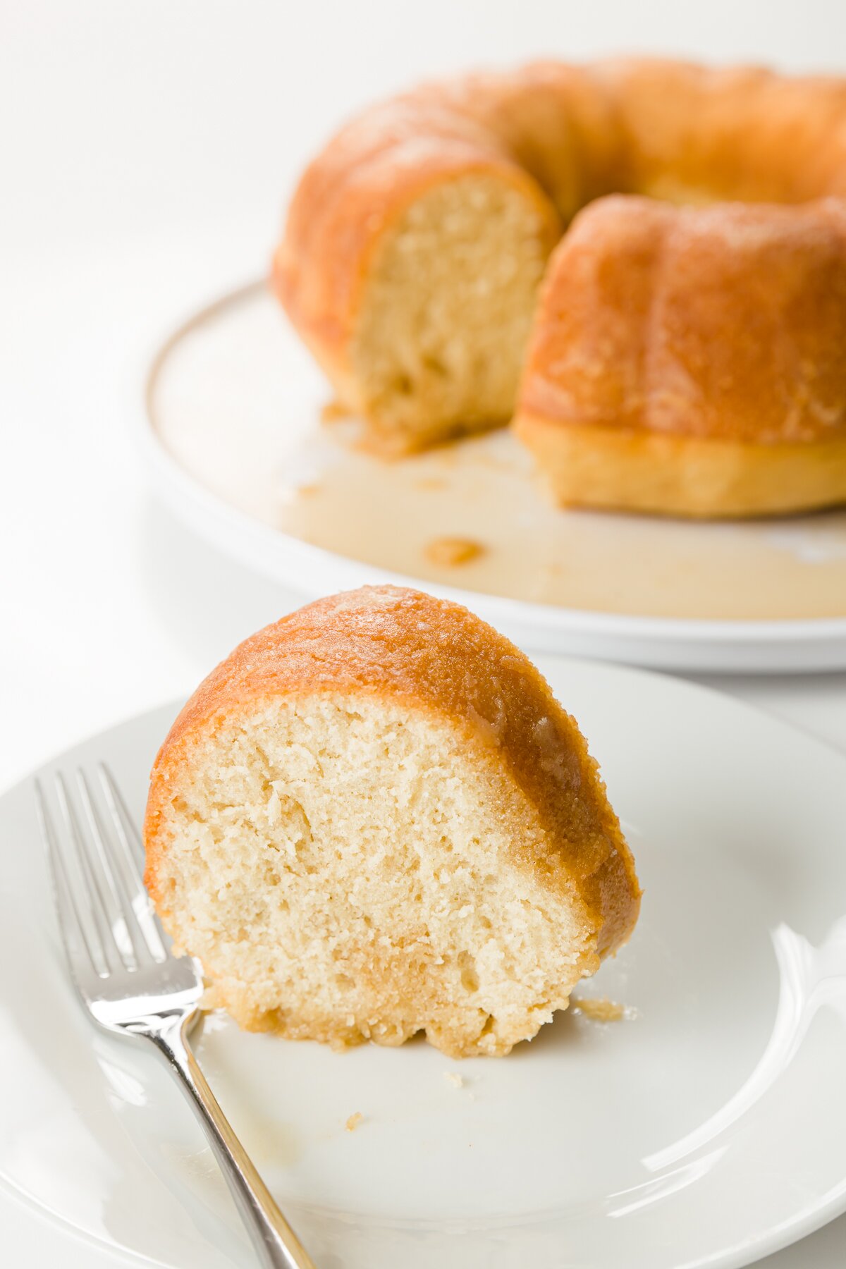 tight shot of a slice of rum cake on a plate with the remainder of the cake in the background