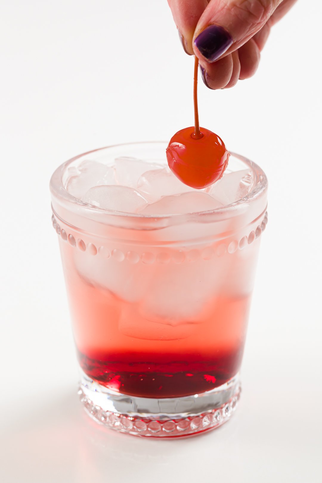 Adding a Maraschino cherry to a Shirley Temple non-alcoholic cocktail placing a Maraschino cherry into a Shirley Temple non-alcoholic cocktail