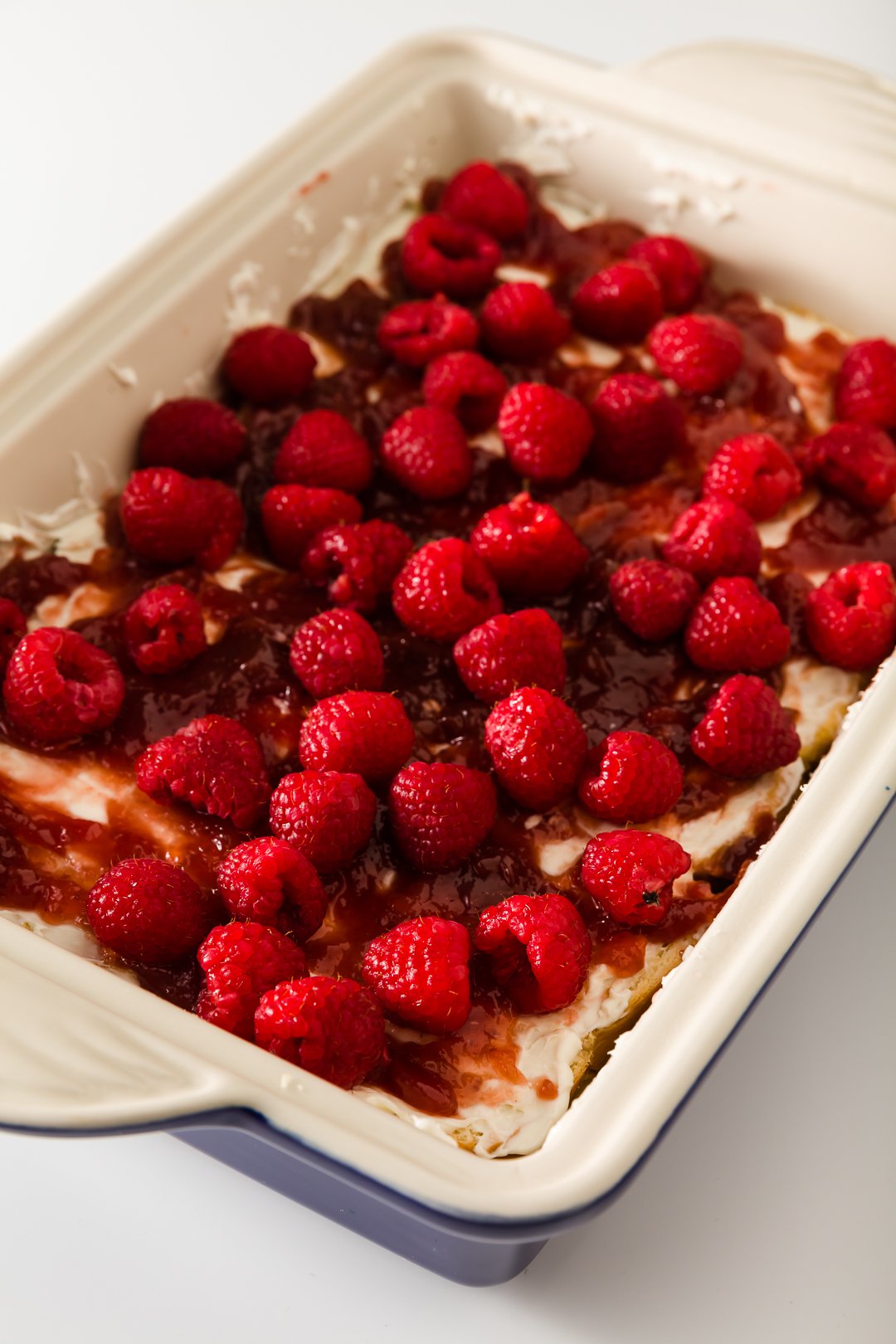 cream cheese, raspberry jam, and raspberries on top of bread in casserole dish 