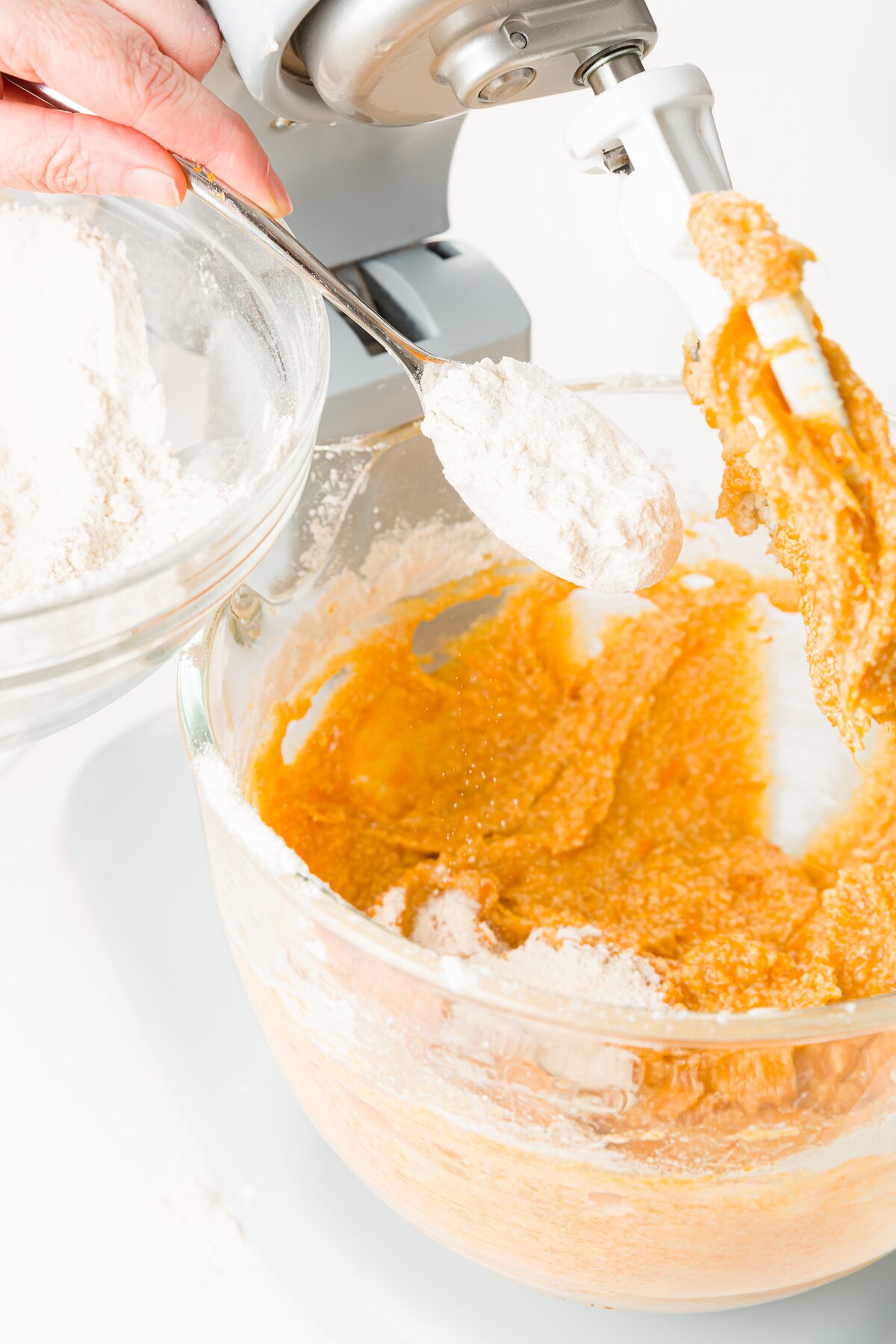Adding flour from a spoon to batter in a KitchenAid mixer