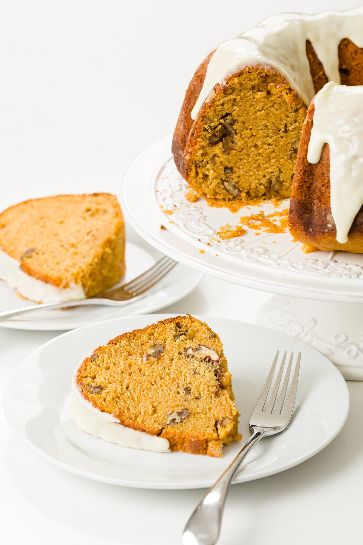 Glazed sweet potato cake on a cake stand with several pieces on white plates in front of it