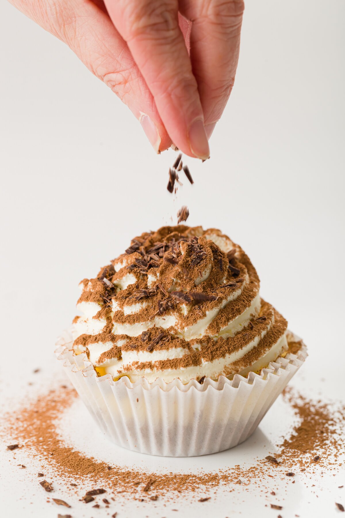 tight shot of Stef adding chocolate shavings to the top of a tiramisu cupcake