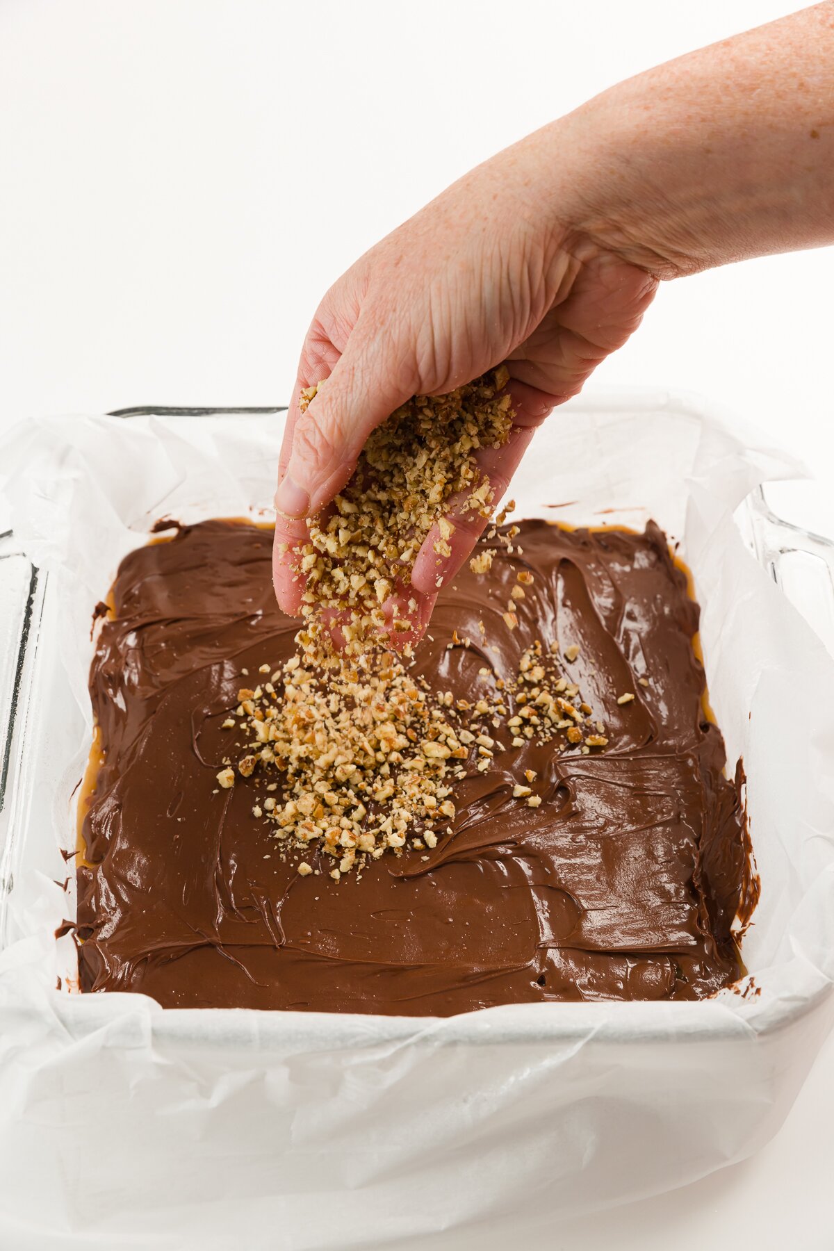 Sprinkling nuts over melted chocolate in square baking dish