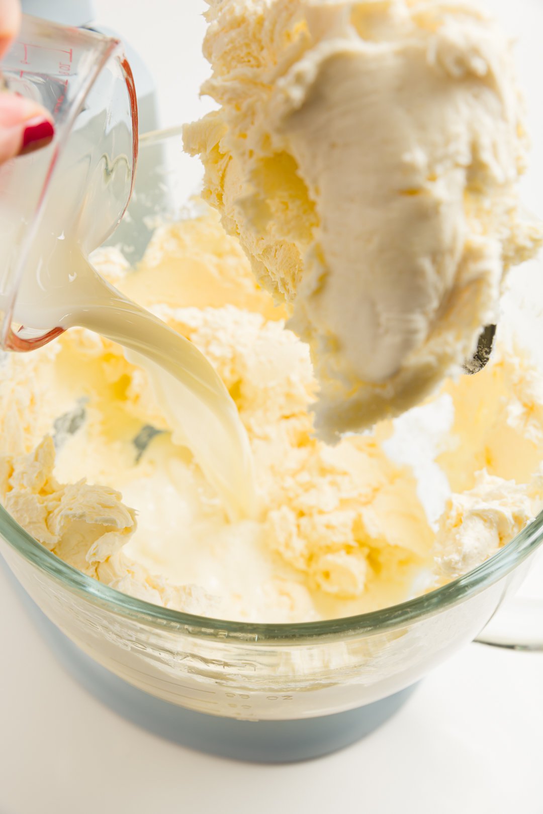 looking into a stand mixer where milk is being added to thoroughly mixed cream cheese and sugar